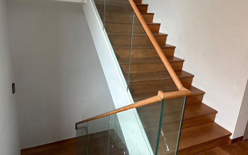 A modern staircase featuring a sleek wooden handrail paired with glass panels A modern staircase featuring a sleek wooden handrail paired with glass panels